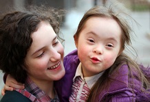 girl with Down Syndrome looking at the camera while being held by another girl who is looking at her